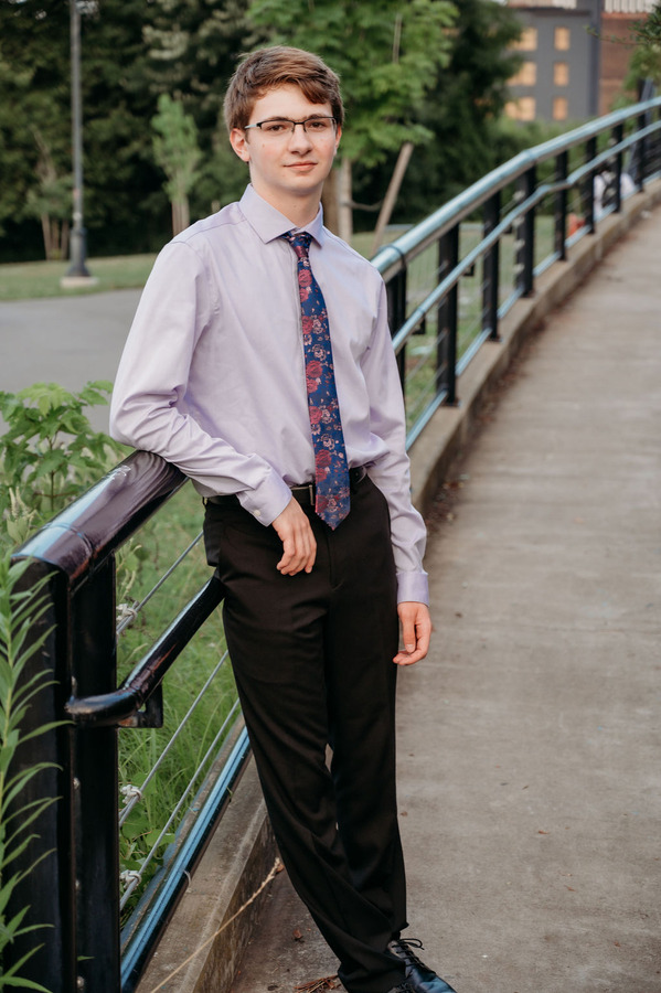 Logan in a shirt and tie leaned against a railing